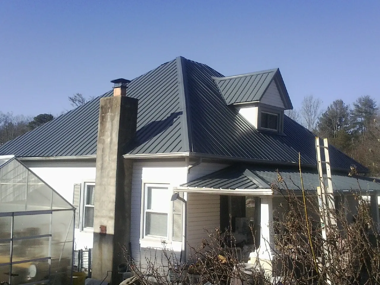 Dark blue standing seam metal roof on a white farmhouse with dormer in Delano