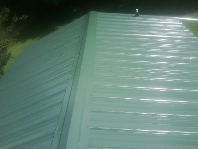 New green metal panels meeting at the ridge of a roof — Flat Roof Repair work by our crew in Delano