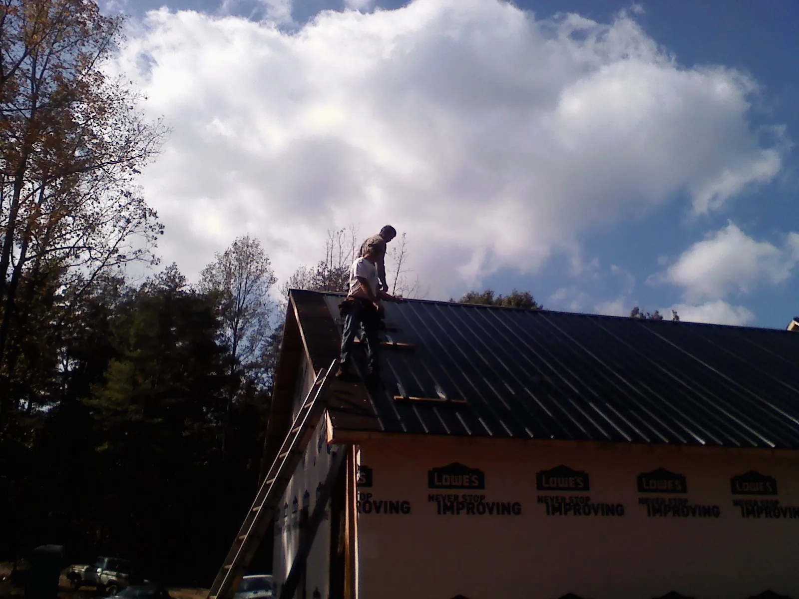 Roofer fastening dark metal panels high against a cloudy sky, from a Roof Inspection job in Delano